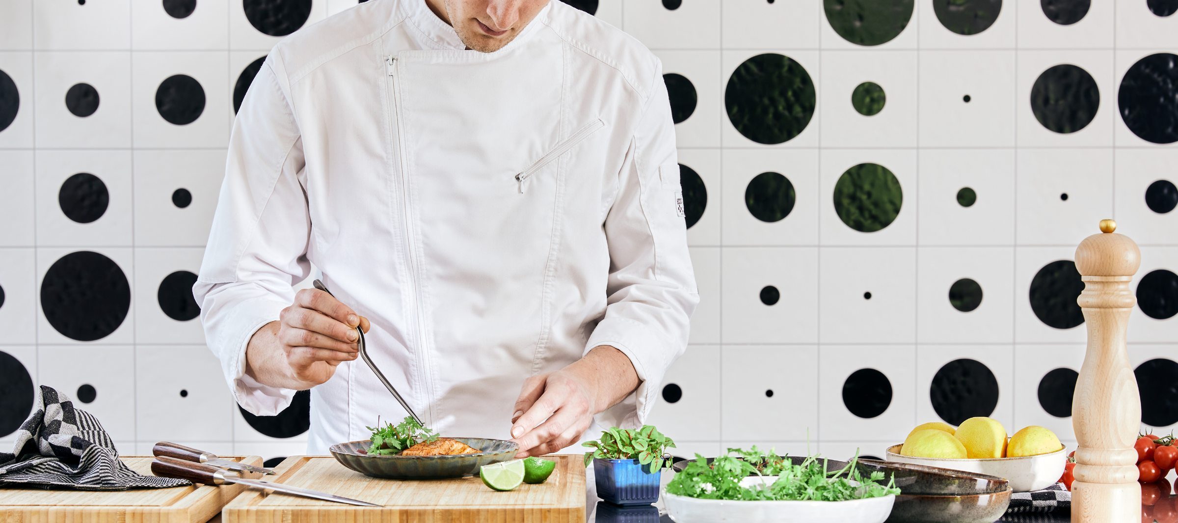 A chef plating a dish against a black-and-white polka-dot tiled wall at Down Under